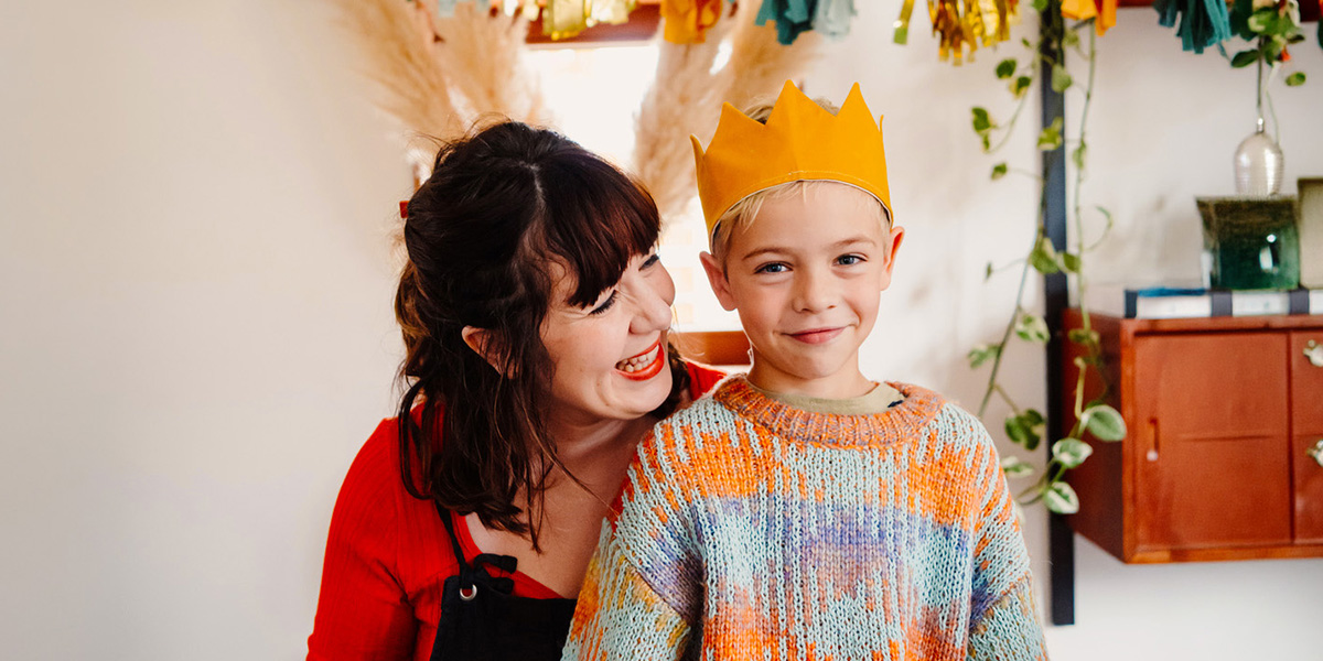 A smiling young boy wears a birthday crown while an older woman smiles at him, illustrating Photobox's ultimate birthday photoshoot checklist.