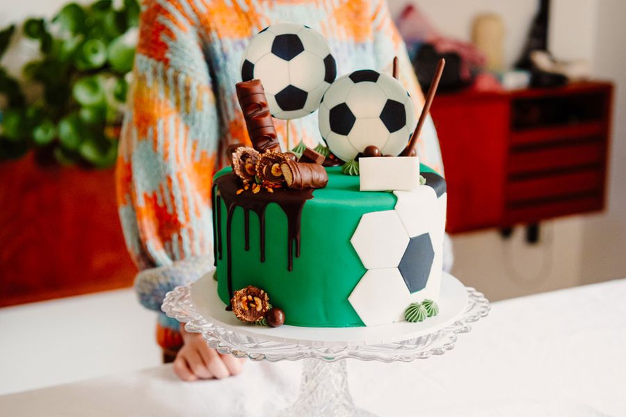 A child's birthday cake decorated with footballs and chocolate bars, illustrating Photobox's tip to photograph the showstopper cake before guests arrive.
