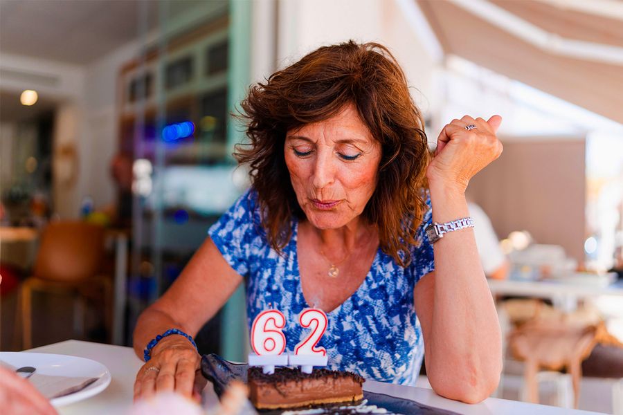 A woman blows out candles reading '62' on her birthday cake, illustrating Photobox's tip to capture the exact moment the candles get blown out.