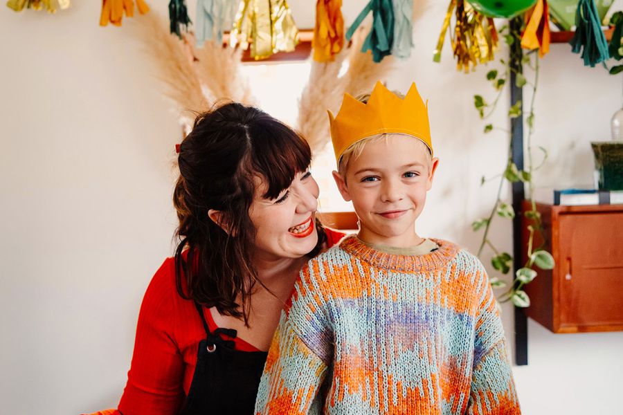A smiling young boy wears a birthday crown while an older woman smiles at him, illustrating Photobox's ultimate birthday photoshoot checklist.