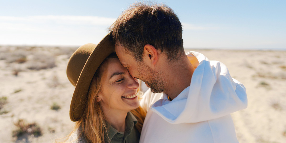 A couple in their 30s smile and embrace in a beachy, desert-like setting, introducing Photobox's guide to 60 anniversary card message ideas.