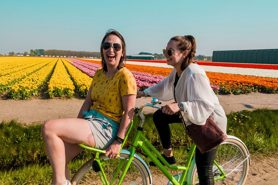 Two women ride a bike together, smiling and laughing in a field full of flowers, illustrating Photobox's ideas for what to write in an anniversary card for friends.