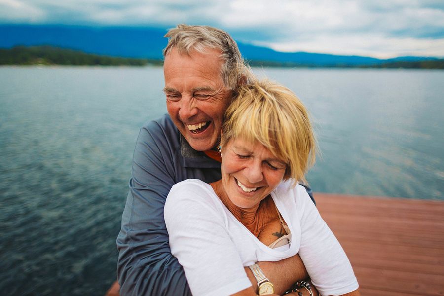 An older couple embraces and smiles near a beautiful lake, illustrating Photobox's ideas for what to write in a milestone anniversary card.