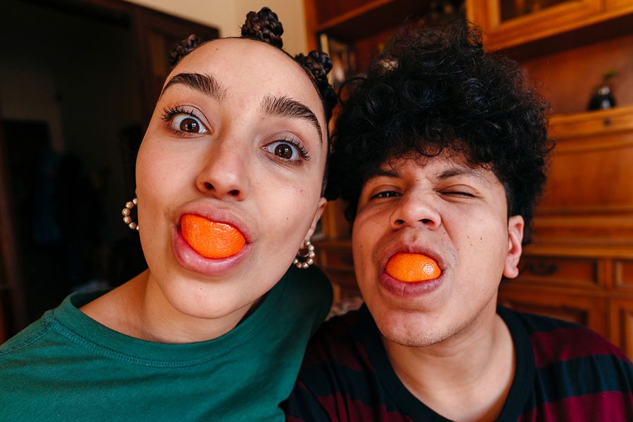 A couple makes funny faces with orange slices in their mouths, illustrating Photobox's ideas for funny things to write in an anniversary card.