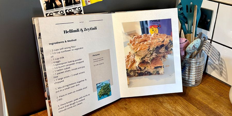 An open personalised recipe book sits in a kitchen setting, with a jar of spoons and cooking utensils in the background, introducing Photobox's guide to making your own cookbook.