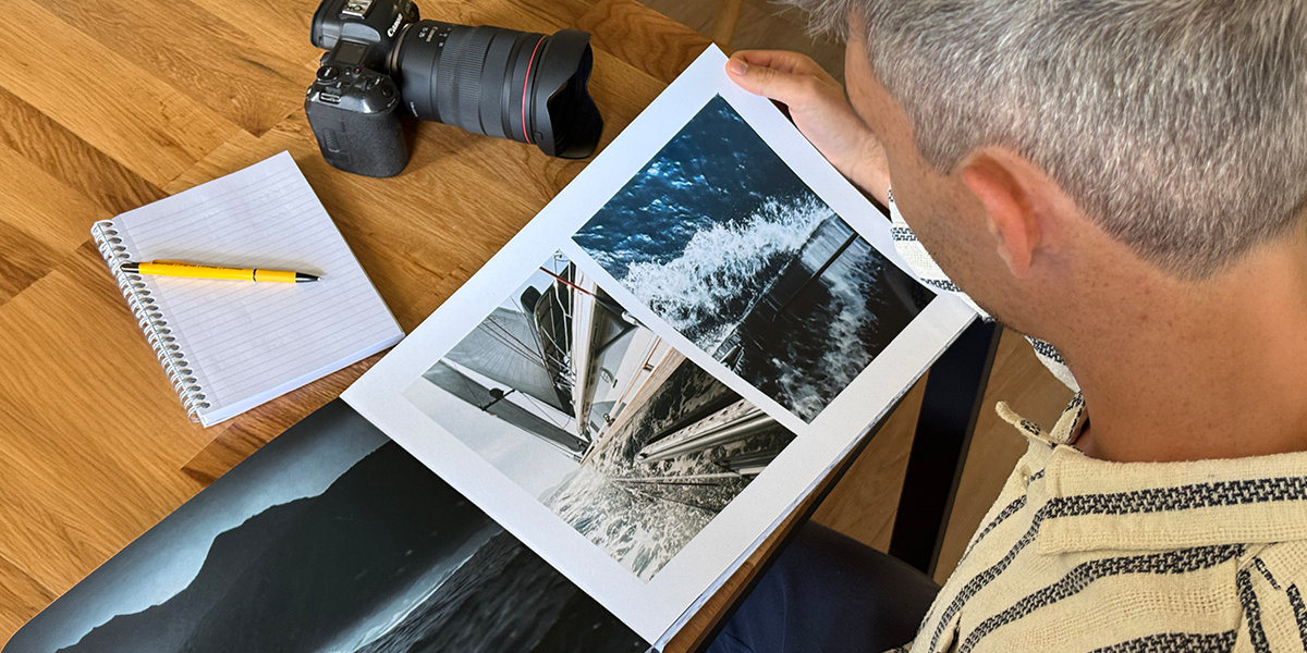 Photographer Charl van Rooy looks down at his portfolio, with his camera and a notebook on the table beside him, introducing Photobox's guide to building a photography portfolio photo book.
