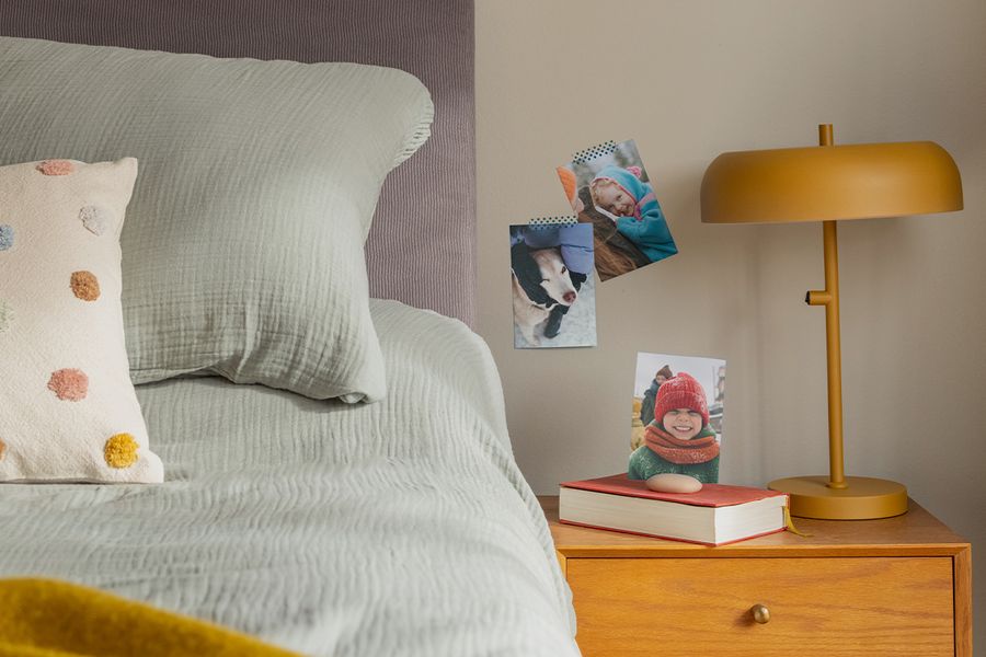 A selection of family photo prints hangs on the wall next to a bed, illustrating how Photobox photo prints add a cosy, personal touch to a hygge bedroom.