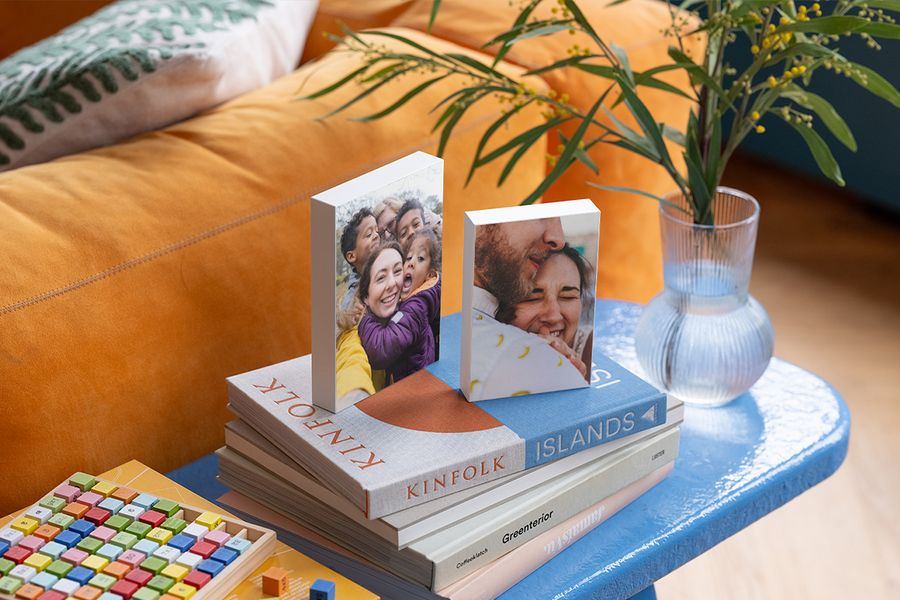 Two personalised photo blocks rest on a selection of coffee table books on a blue side table next to an orange velvet sofa, illustrating how Photobox photo blocks add a personal touch to a hygge home.