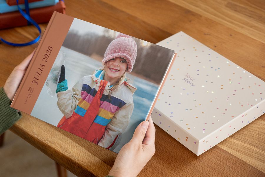 Someone holds a photo book titled 'Julia', featuring a smiling girl on the cover, with a presentation gift box resting on the table just behind it, illustrating why a photo book box makes a creation feel extra special.