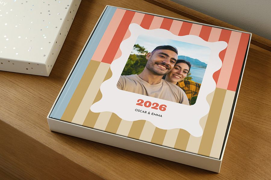 A photo book rests inside the gift box with the lid off, appearing to be a yearbook labelled '2026' with a smiling couple on the cover, illustrating how to choose the right presentation box size for your photo book.
