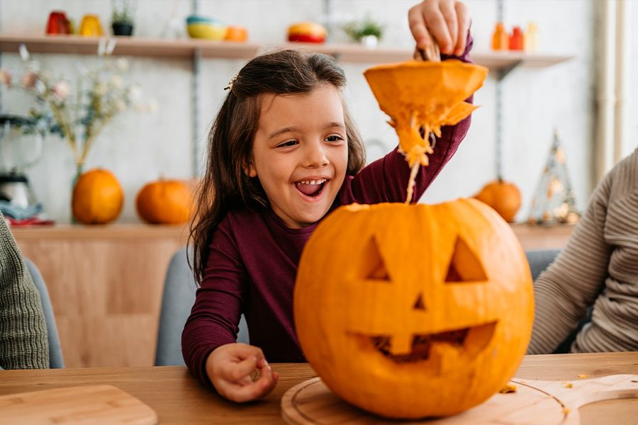 A child pulls the top off a pumpkin they have just carved, illustrating Photobox's funny and cute pumpkin sayings for Halloween Instagram captions.