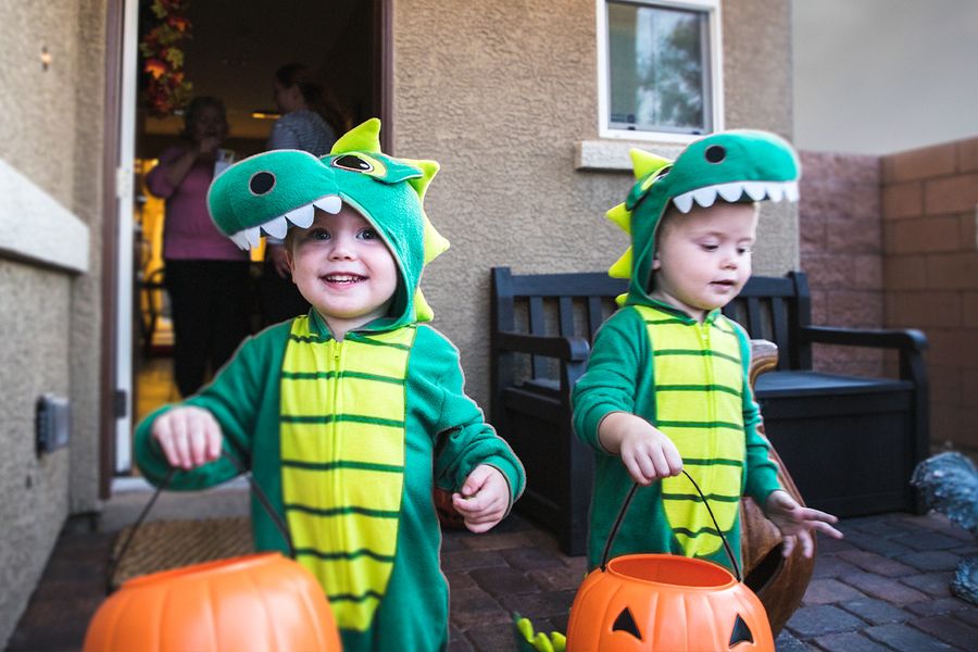 Two little boys in dinosaur costumes go trick or treating, holding pumpkin baskets, illustrating Photobox's Halloween captions for trick-or-treating photos.