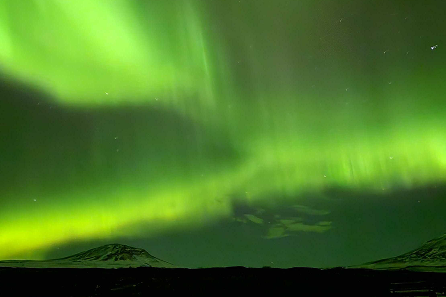 Snowy mountains under a sky turned very green by the northern lights, illustrating Photobox’s tips on where to see northern lights without going to Iceland.