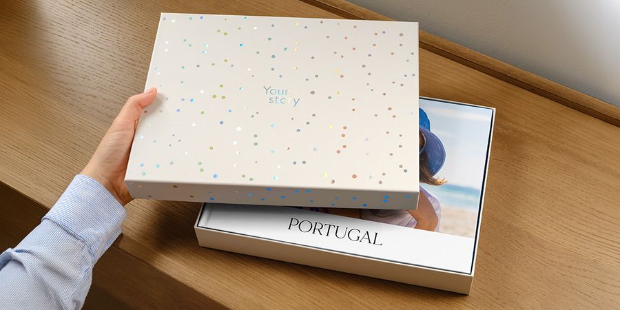 A Photobox presentation box sits with its lid ajar, revealing a personalised travel photo book for Portugal inside, its cover image partially obscured by the lid, introducing Photobox's new photo book gift box.