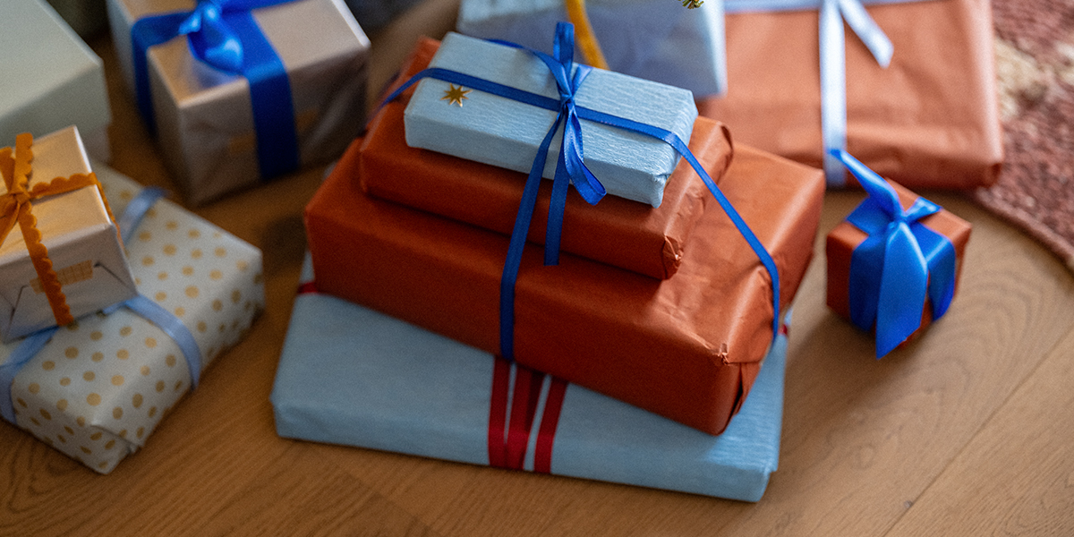A stack of presents wrapped in orange and pale blue paper and tied with blue ribbons on a wooden floor, illustrating Photobox’s Black Friday Christmas gifts to buy this year.