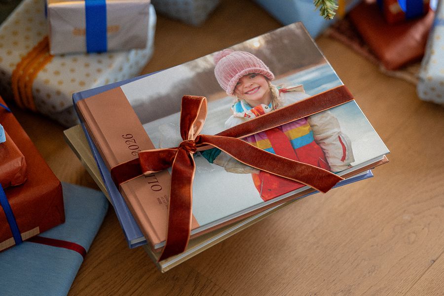 Stack of personalised photo books tied with a brown velvet ribbon, with other wrapped gifts in the background, illustrating Photobox’s tips on preparing a personalised photo gift for Christmas.