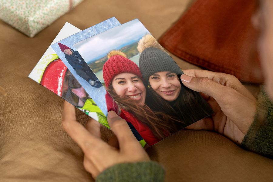 Person holding photo prints in their hands, with the front print showing two smiling women in winter hats and coats, illustrating Photobox’s tips on finding the right photos for a personalised photo gift.