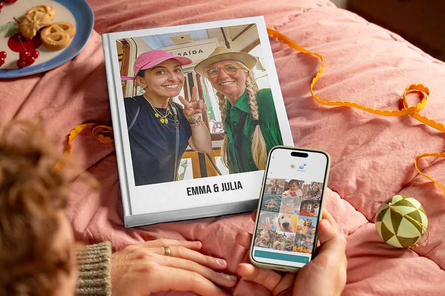 Personalised photo book called “Emma and Julia” with a mother and adult daughter on the cover, next to a man’s hands holding a phone to show how easy it is to select photos to create a Photobox photo book, illustrating Photobox’s tips on gathering photos from family and friends for a personalised gift.