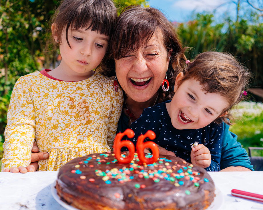 Grandma with her two grandkids happily blowing out birthday candles.