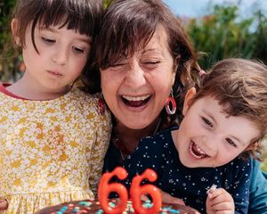 A grandmother celebrates her 66th birthday with her two grandchildren beside her, about to blow out the candles on her cake, inspiring birthday gift ideas from the Photobox ultimate birthday gift guide.