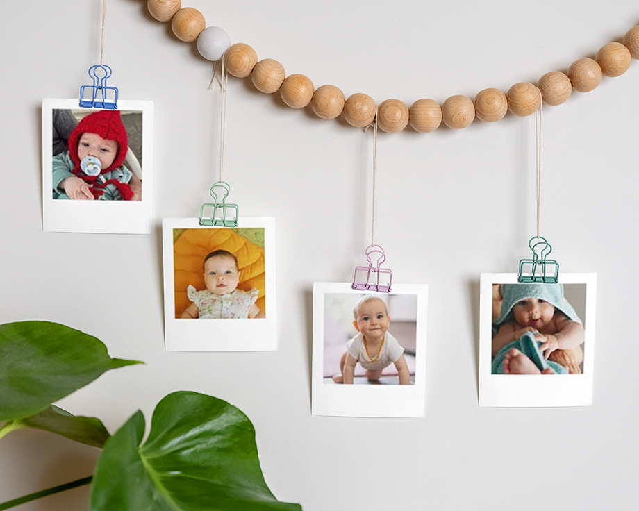 Baby photos clipped to a wooden bead garland hanging on a wall.