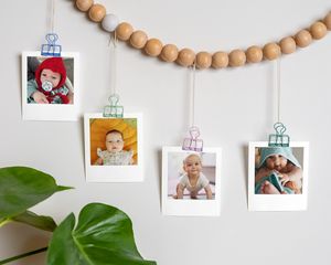 Baby photos clipped to a wooden bead garland hanging on a wall.