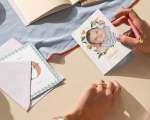 Hands writing a personalised baby photo card at a desk.