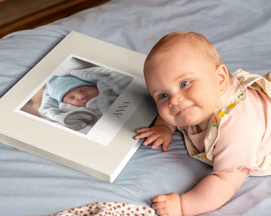 Baby lying next to a personalised photo book with a baby picture on the cover.