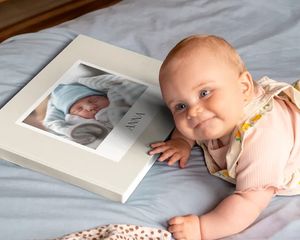 Baby lying next to a personalised photo book with a baby picture on the cover.