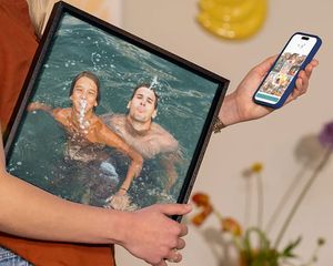 A woman holding Photobox wall art featuring a family playing in the water on holiday, inspiring ideas for turning holiday photos into stunning wall art.